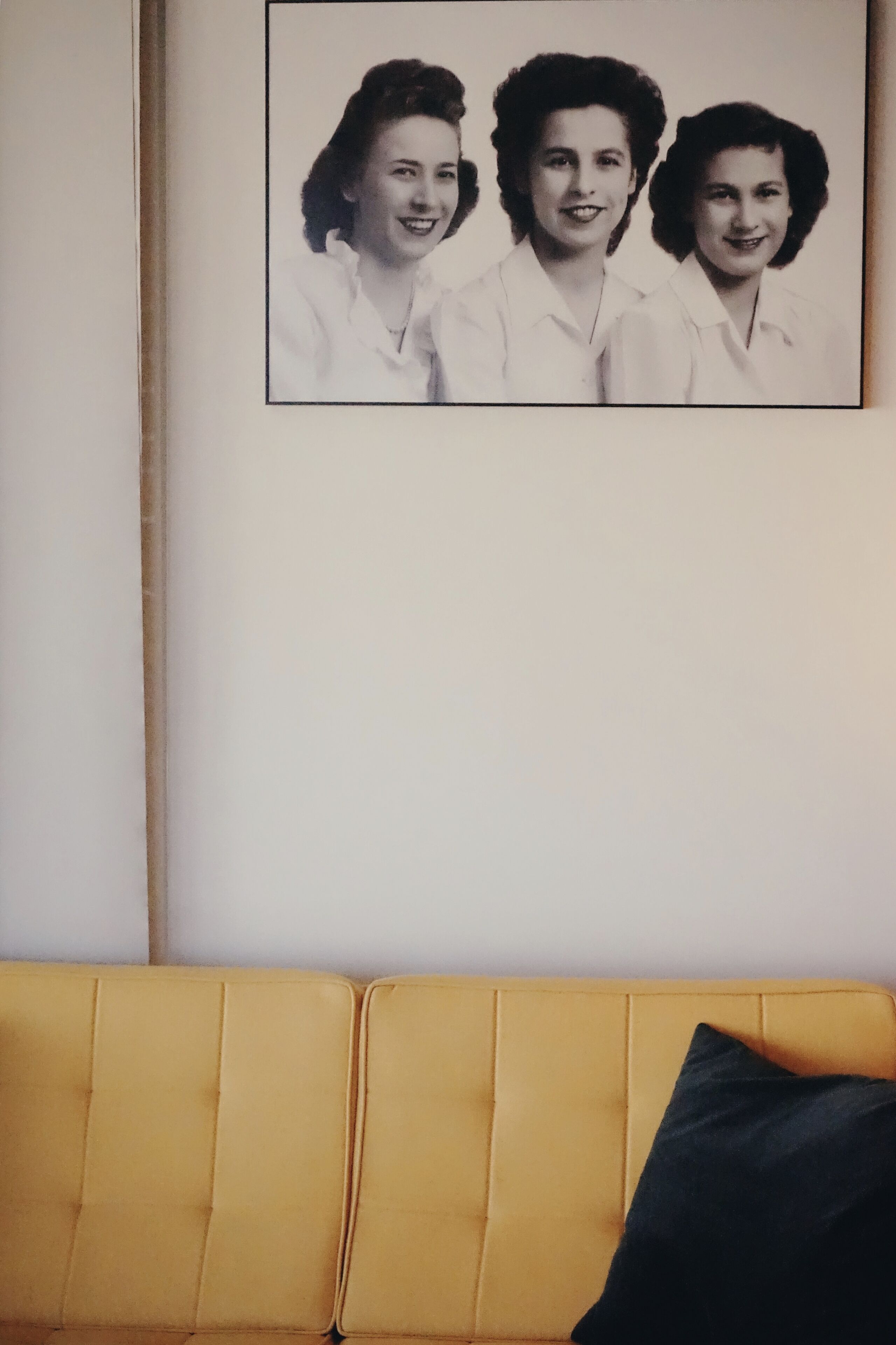 Une photographie en noir et blanc, encadrée, est accrochée au mur au-dessus d’un canapé jaune.