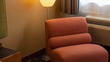 Ein Hotelzimmer mit einem einzelnen rosa Sessel, einer Stehlampe und einem Bett mit einer farbenfrohen Steude.