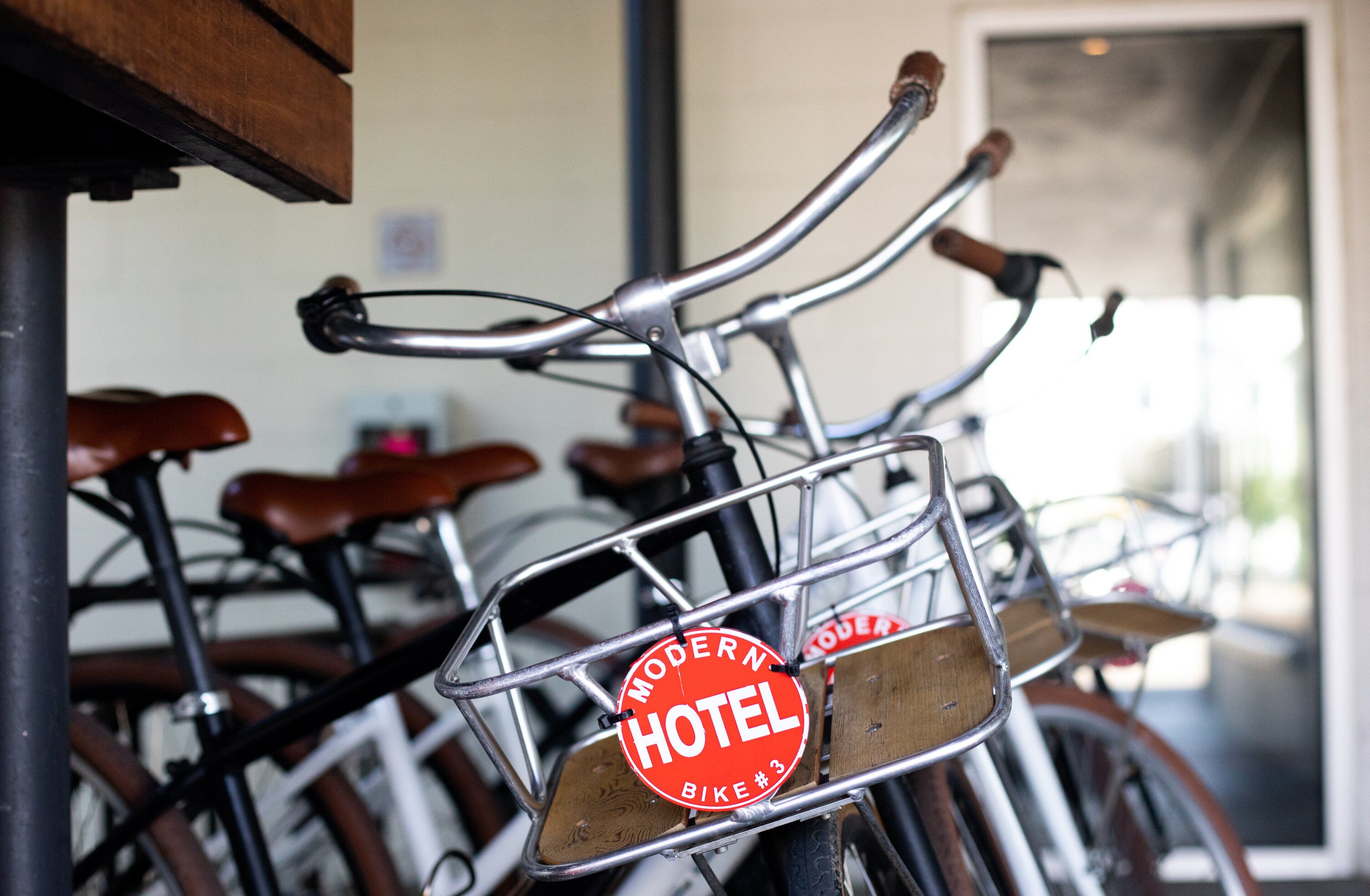 A bicycle with a metal basket and a wooden seat, labeled "Modern Hotel Bike #3".