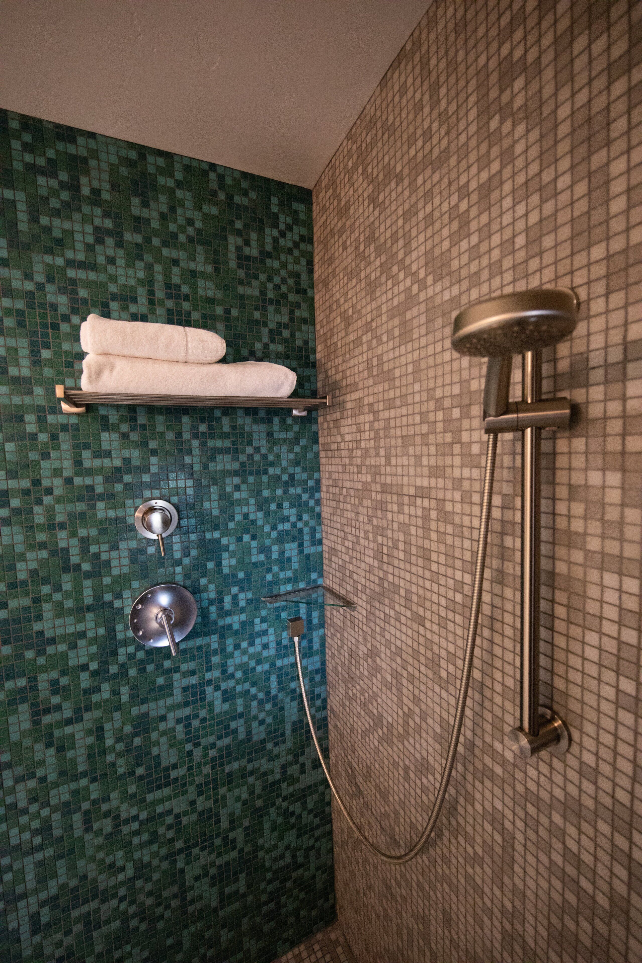 Un bagno con parete rivestita in mosaico, un appendi-asciugamani con asciugamani, un soffione e un doccetta.