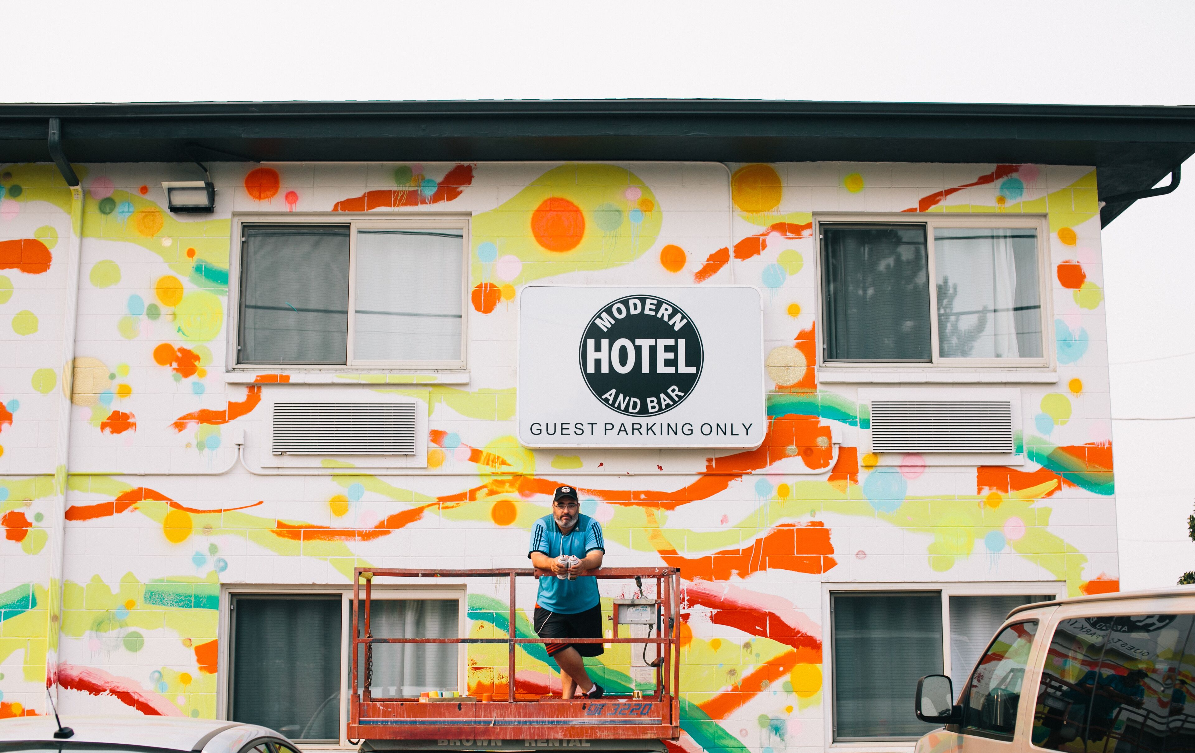 Un bâtiment aux couleurs vives, sur lequel on peut lire l’inscription « Hôtel et bar moderne », et un panneau indiquant « Stationnement réservé aux clients ».