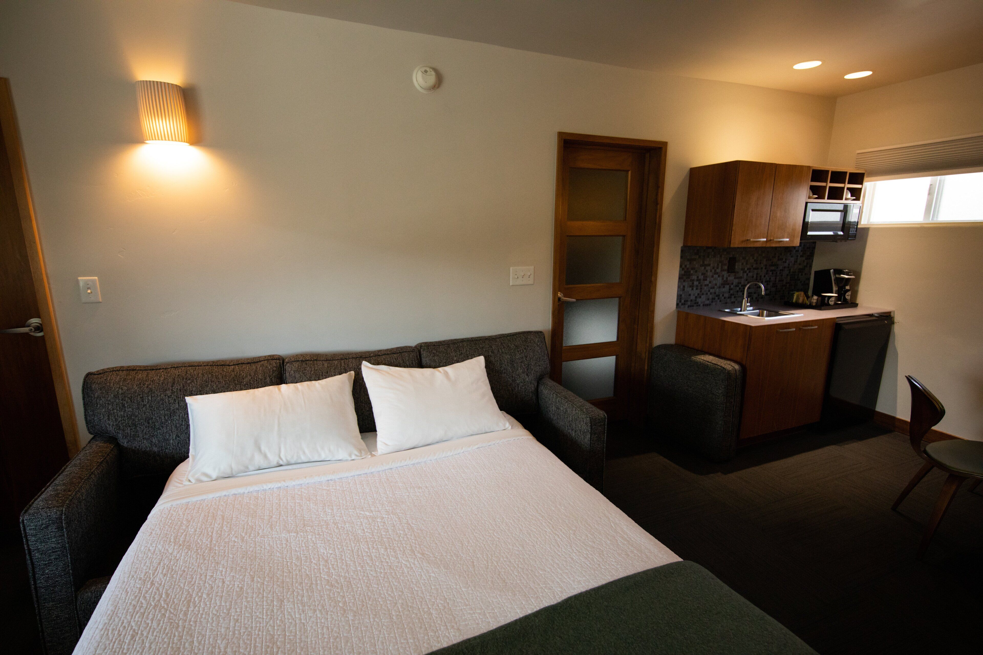 A compact hotel room with a bed, a small desk, and a kitchenette.