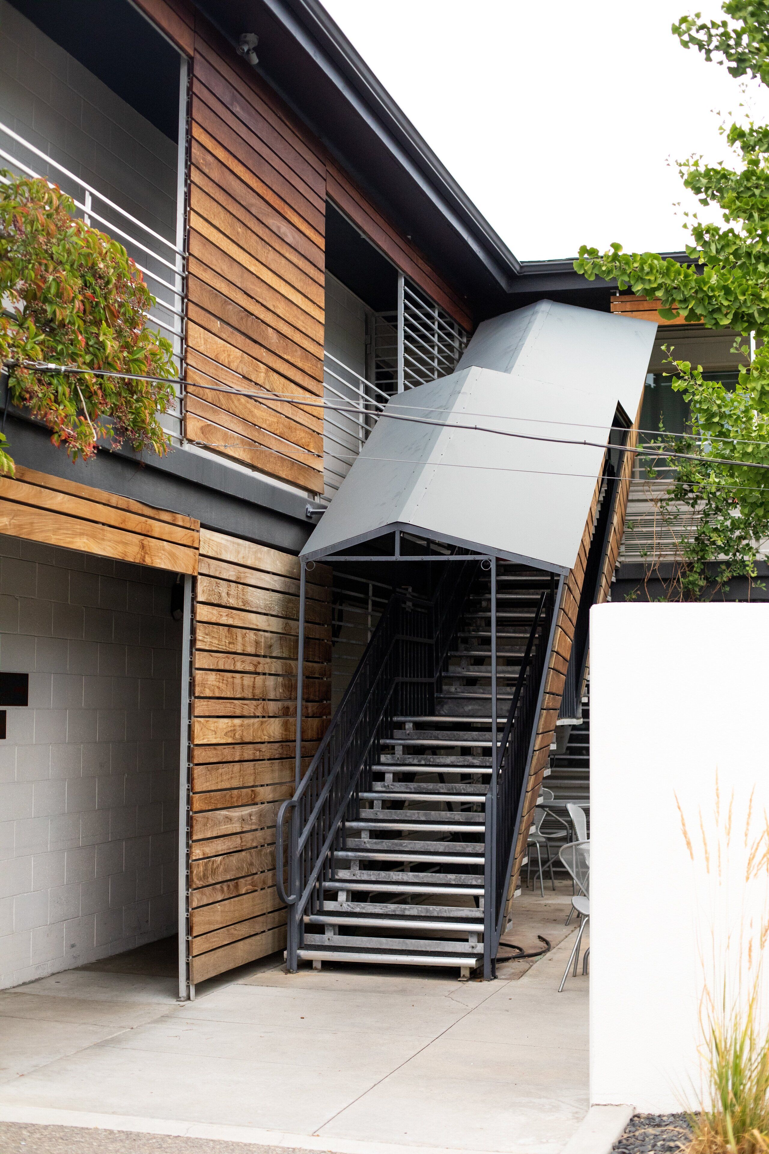 A modern building with a wooden facade, a metal staircase, and a covered outdoor area.