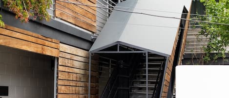 A modern building with a wooden facade, a metal staircase, and a covered outdoor area.
