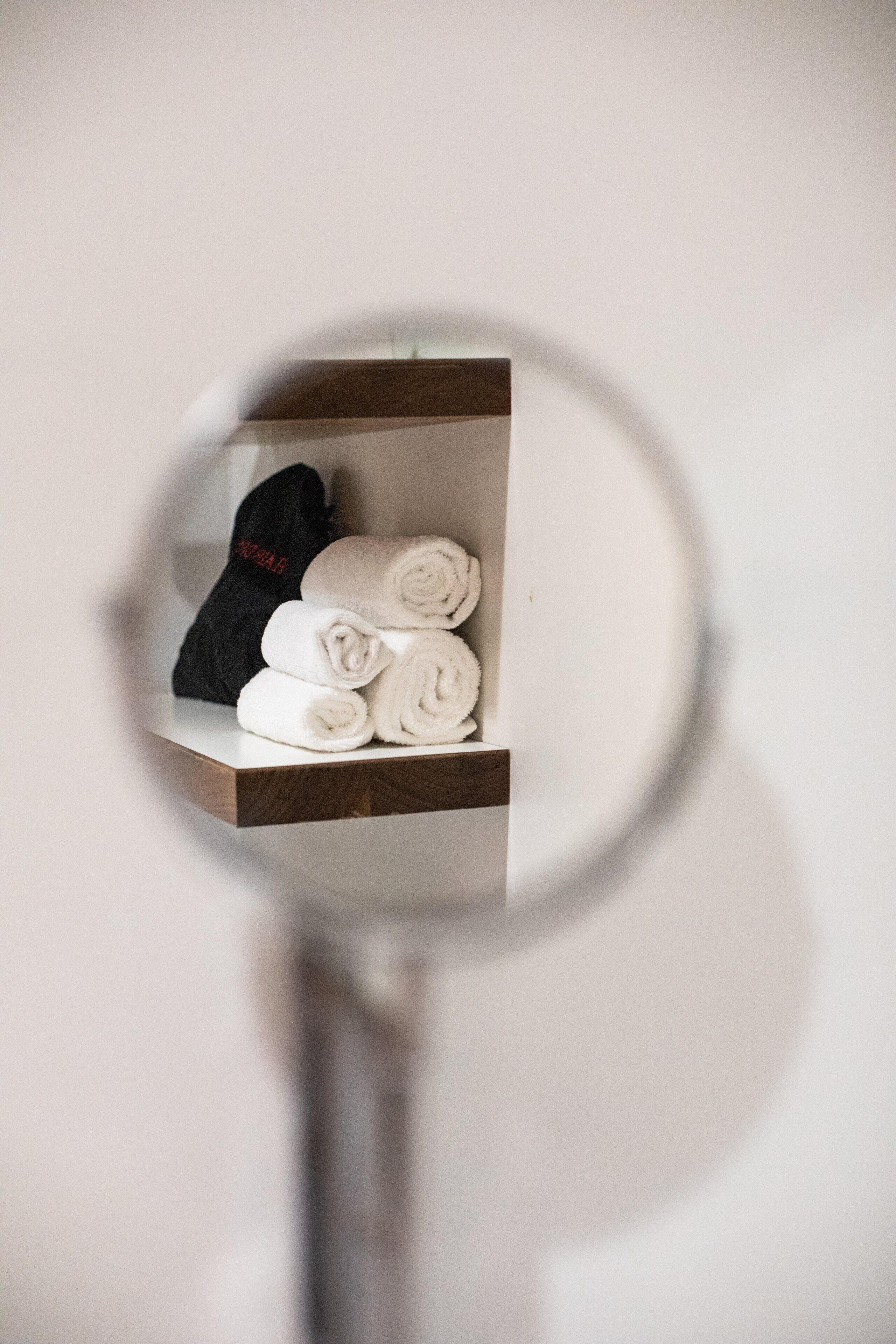 A mirror reflecting a shelf with neatly rolled towels and a black item.