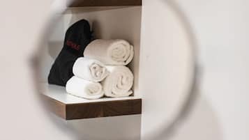 A mirror reflecting a shelf with neatly rolled towels and a black item.