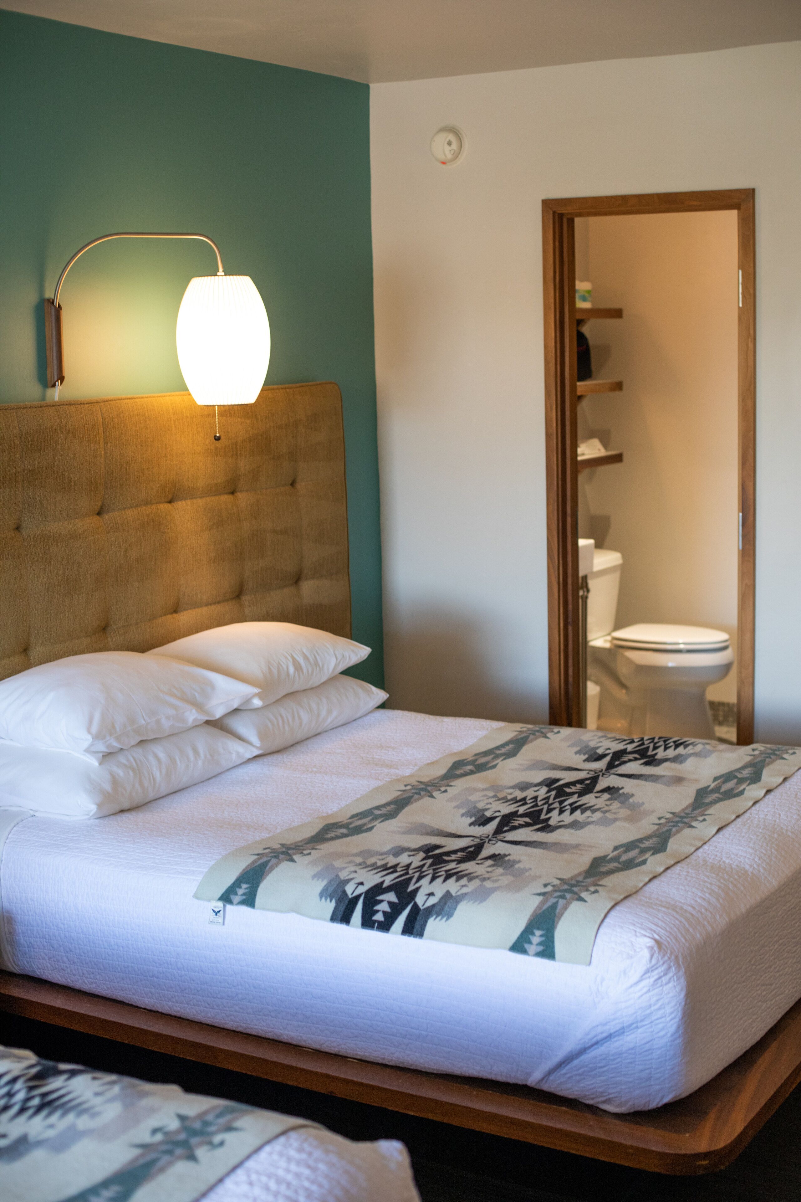 Una cama bien tendida con cabecera, lámpara de noche y una colcha estampada con motivos florales.
