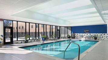 Una piscina interior con paredes de vidrio transparente, suelo de baldosas y una pared azul con un cartel que dice 'No Lifeguard, No Diving'.