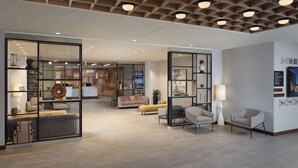Un hall d’entrée spacieux au design moderne, comprenant un espace détente avec des canapés et des fauteuils, un comptoir d’accueil et un plafond décoratif doté d’un éclairage encastré.