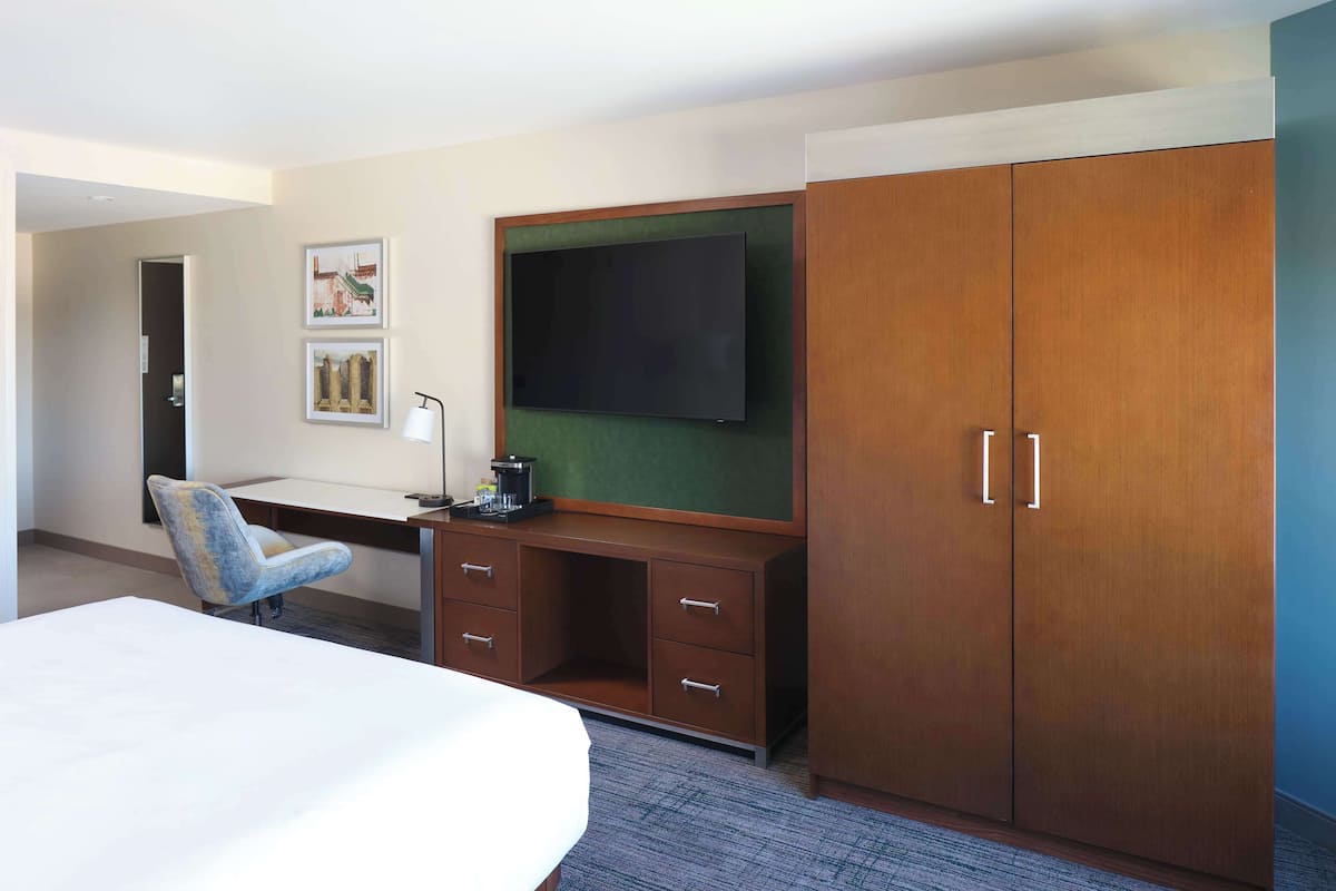 Een hotelkamer met een bed, een bureau met een computer, een stoel, een kledingkast en een televisie.