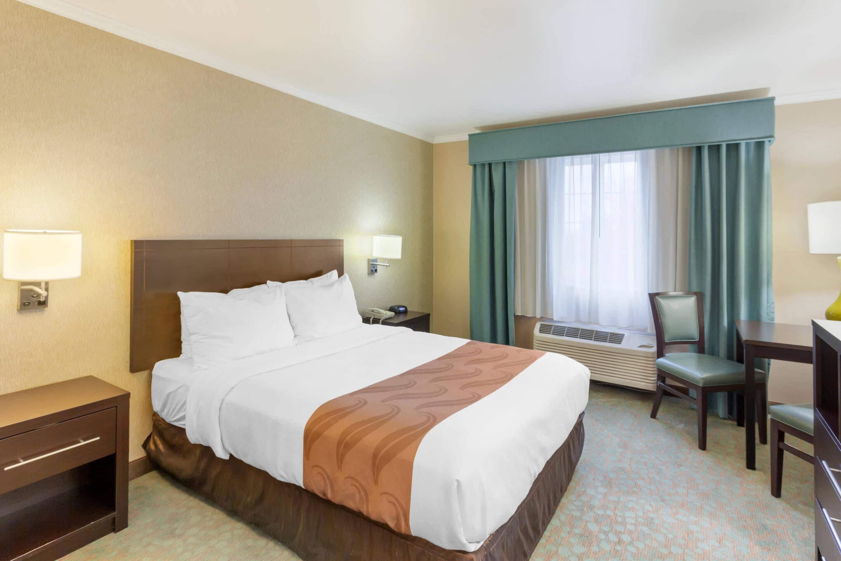 A hotel room with a large bed, bedside tables, a desk, and a chair.