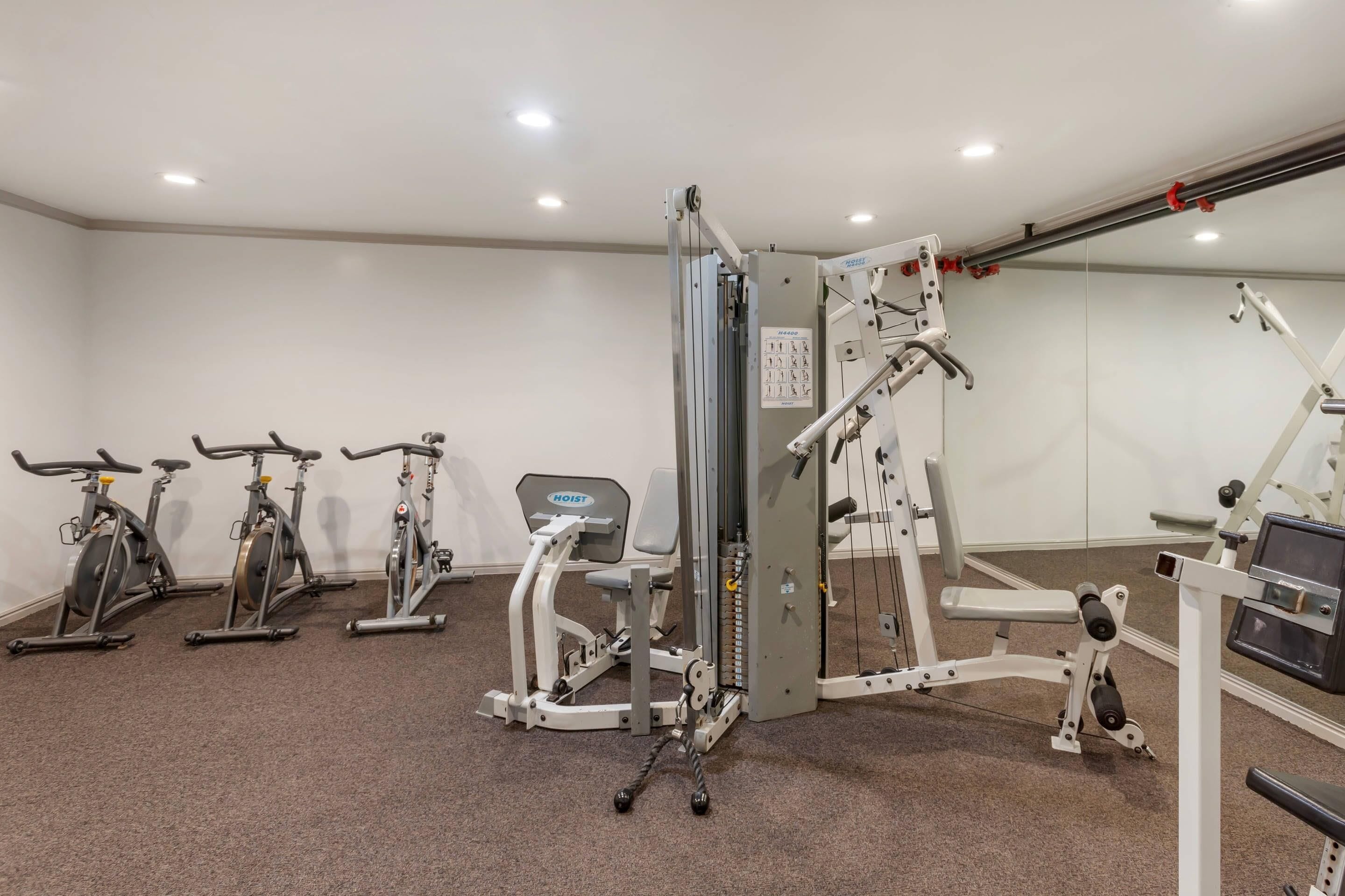 A gym with stationary bikes, a weight machine, and a mirror wall.