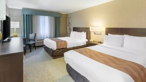 Habitación de hotel con dos camas, un escritorio con lámpara, una silla y un televisor.