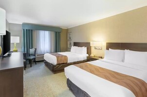 A hotel room with two beds, a desk with a lamp, a chair, and a television.