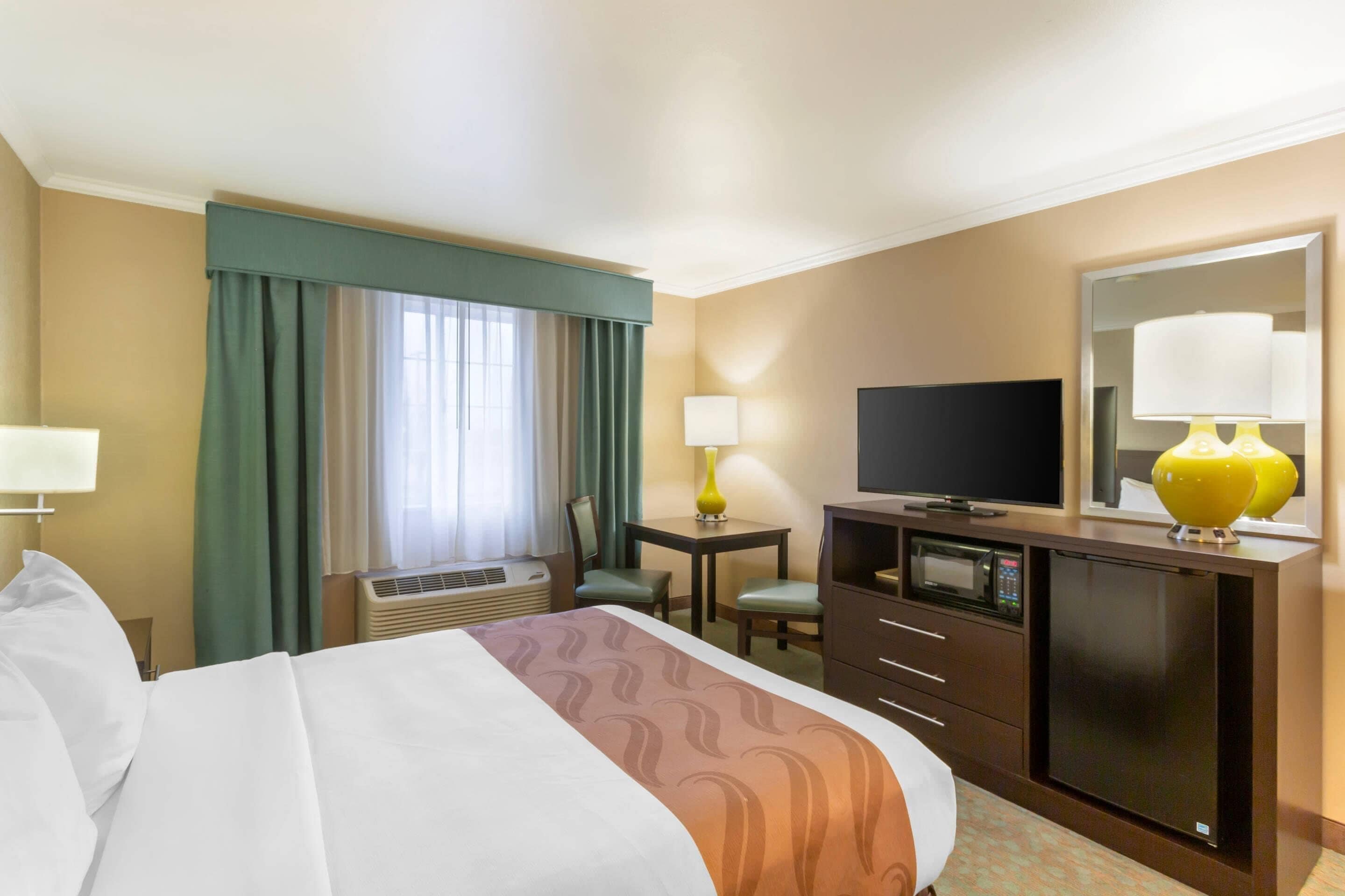 A hotel room with a bed, a desk, a television, a mirror, and a window with curtains.