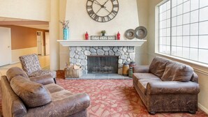 Una sala de estar con chimenea de piedra, sofás de cuero, un reloj de pared grande y una alfombra estampada.