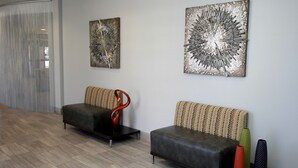 A modern waiting area with two sofas, a glass partition, and abstract wall art. - Plaza Hotel Denver (Denver)