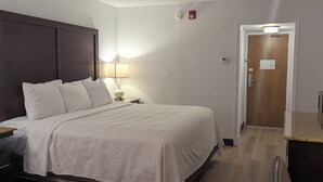 A hotel room with a bed, bedside table, lamp, and a wooden floor. - Plaza Hotel Denver (Denver)