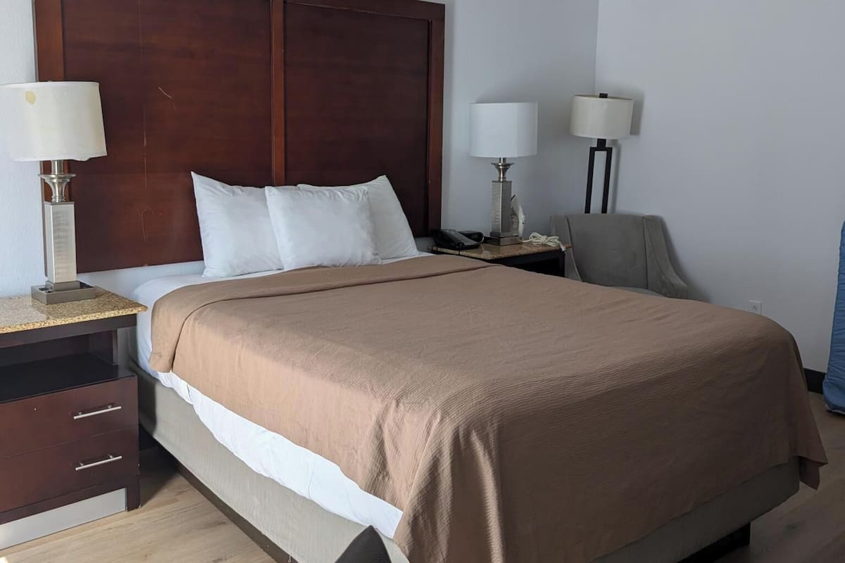 A hotel room with a large bed, two bedside tables with lamps, a chair, and a wooden floor.