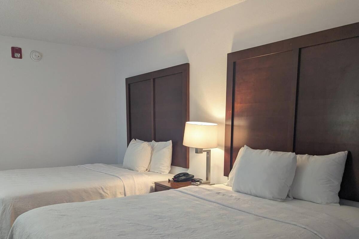 A hotel room with two beds, a nightstand with a lamp, and a wooden headboard.