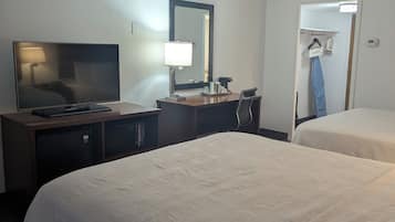 Quarto de hotel com duas camas, uma mesa com televisão, um espelho e uma porta para uma casa de banho com porta-toalhas.