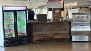 A coffee shop with a wooden counter, a refrigerated display case with beverages, a coffee machine, and a menu board. - Plaza Hotel Denver (Denver)