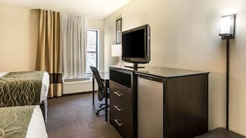 Een hotelkamer met een bed, een bureau met een computer, een stoel, een lamp en een raam met gordijnen.