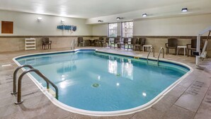 A swimming pool with a tiled floor, surrounded by chairs and tables, and a sign indicating the pool area. - Comfort Inn Wings Stadium (Kalamazoo)
