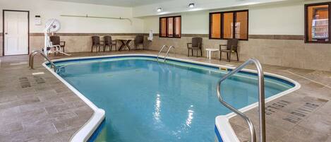 An indoor swimming pool with a tiled floor, metal pool ladders, and a seating area with chairs and tables.