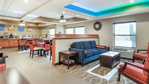 A hotel lobby with a kitchen area, seating with red chairs, a blue sofa, and a clock on the wall. - Comfort Inn Wings Stadium (Kalamazoo)