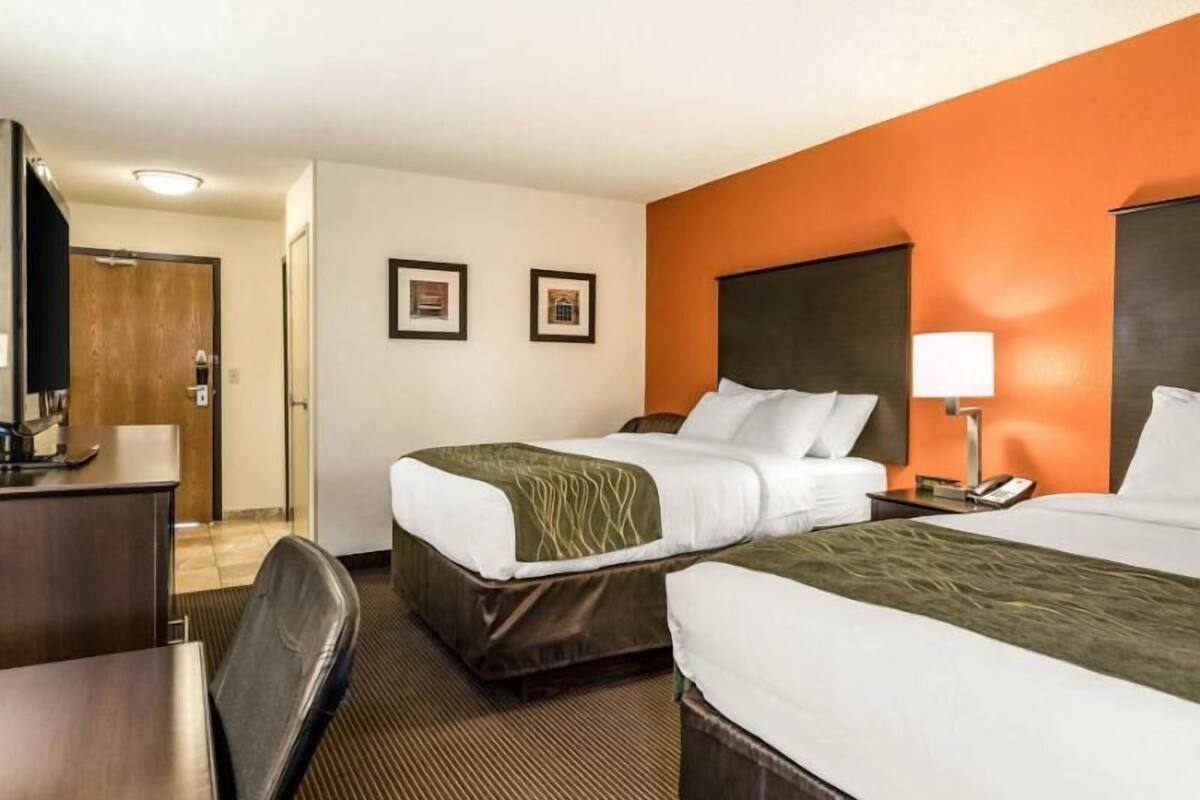 A hotel room with two beds, a desk, a chair, and a television.