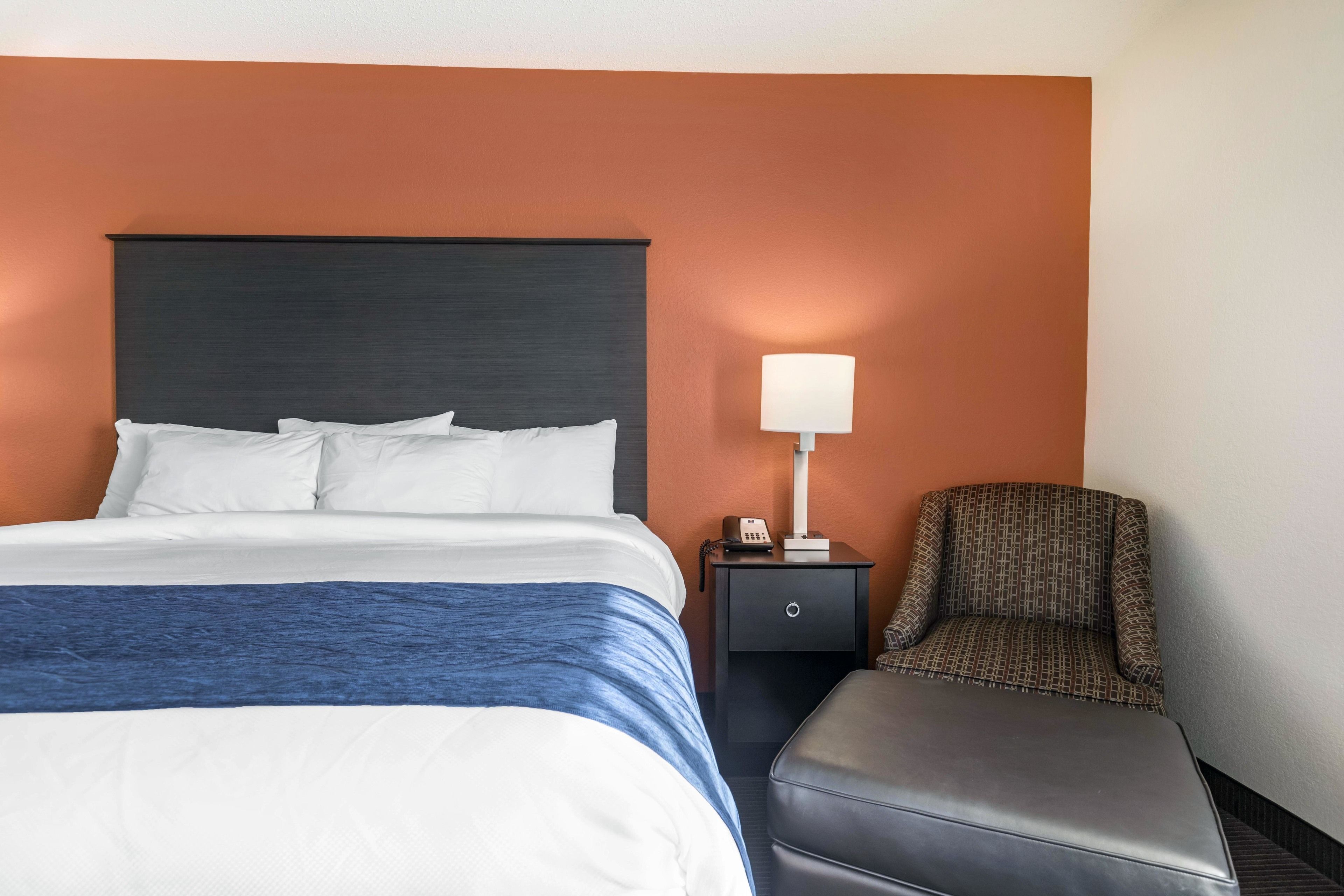 A hotel room with a bed, a nightstand with a lamp, and a chair.