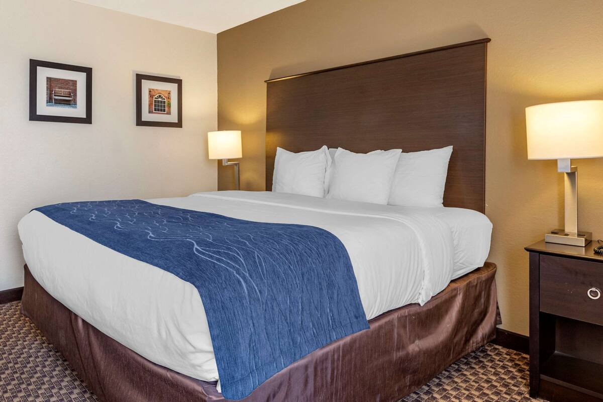 A hotel room with a large bed, two wall-mounted lamps, and a framed picture on the wall.