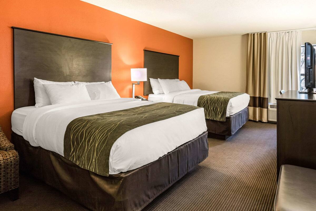 A hotel room with two beds, a desk, a chair, a TV, and a window with curtains.