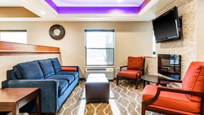 A modern living room with a blue sofa, red armchairs, a coffee table, and a flat-screen TV mounted on a brick wall. - Comfort Inn Wings Stadium (Kalamazoo)