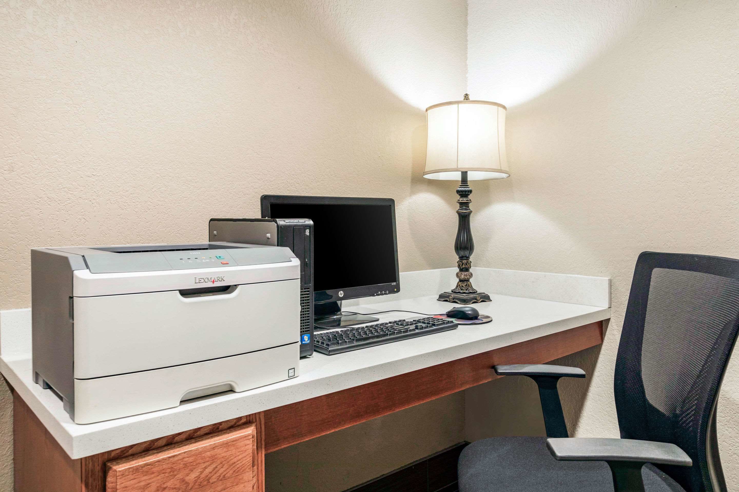 A hotel workspace with a printer, monitor, keyboard, and lamp.
