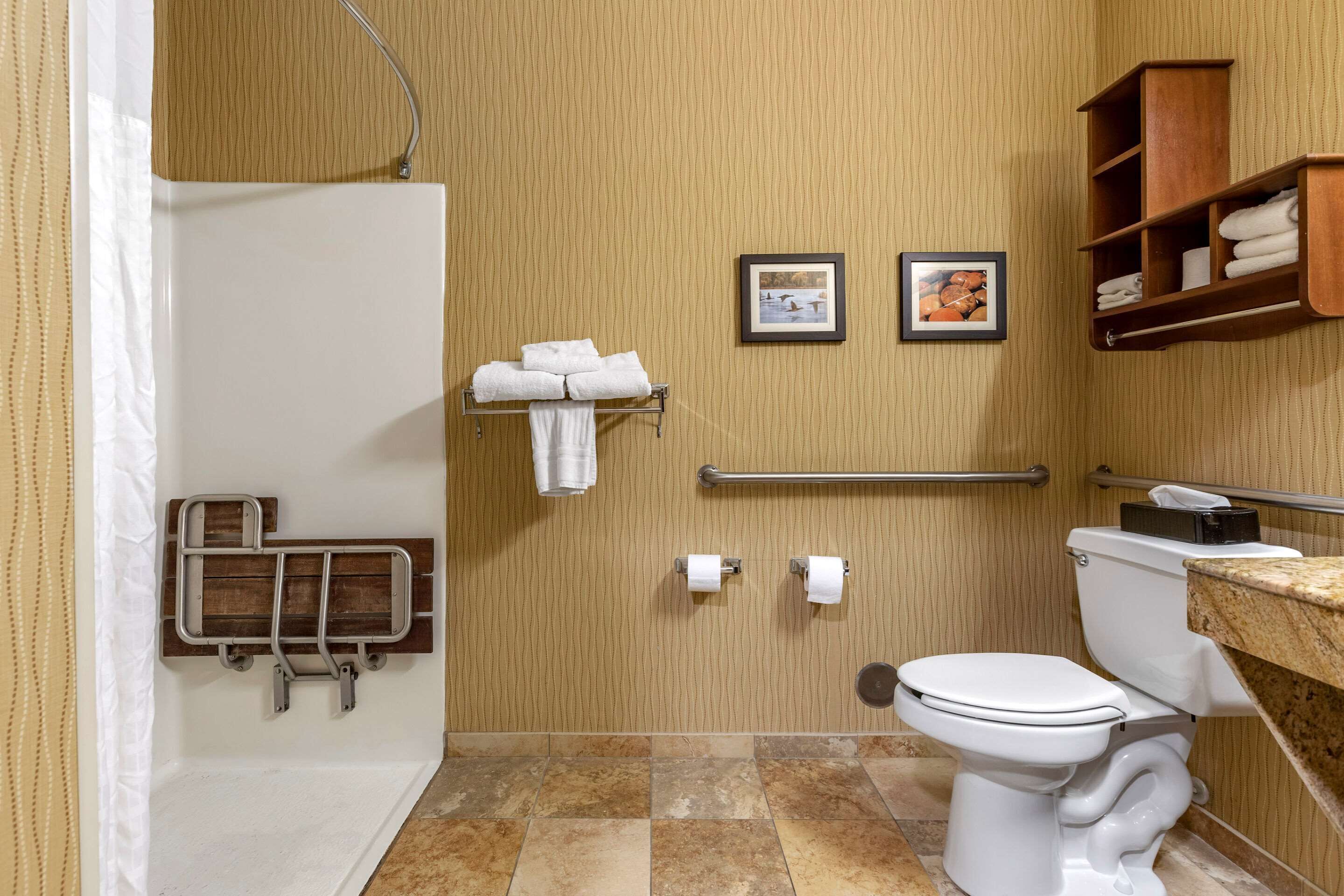 A bathroom with a bathtub, toilet, and a shower area. There are towels and a handrail.