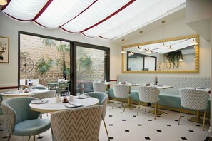 A restaurant interior with round tables, chairs, a stone wall, and a large mirror. - Hôtel des Comédies (Paris)