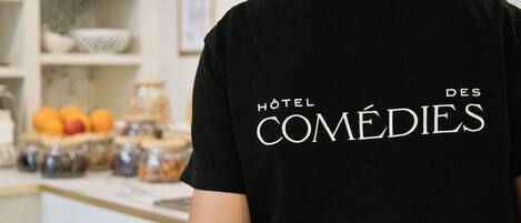 Una persona con camiseta negra que lleva impreso 'Hôtel des COMÉDIES' en la parte de atrás.