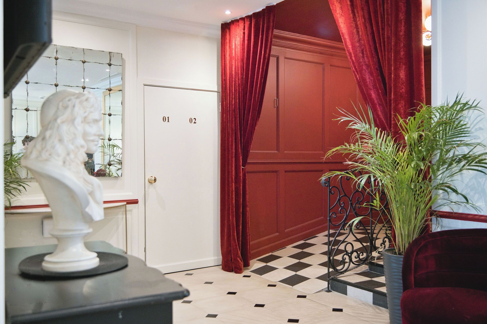 Una habitación con suelo a cuadros, una puerta roja y una escultura de busto sobre una mesa.