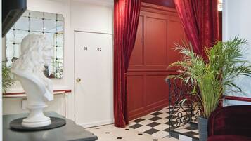 Una habitación con suelo a cuadros, una puerta roja y una escultura de busto sobre una mesa.