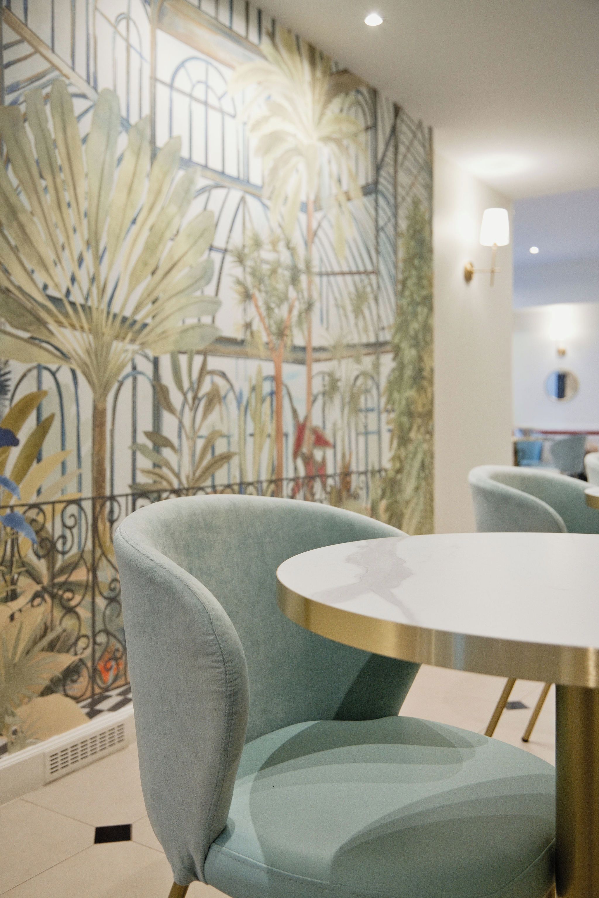 Un interior moderno con una mesa redonda y dos sillas, una pared decorativa con palmeras y una ventana con vistas.