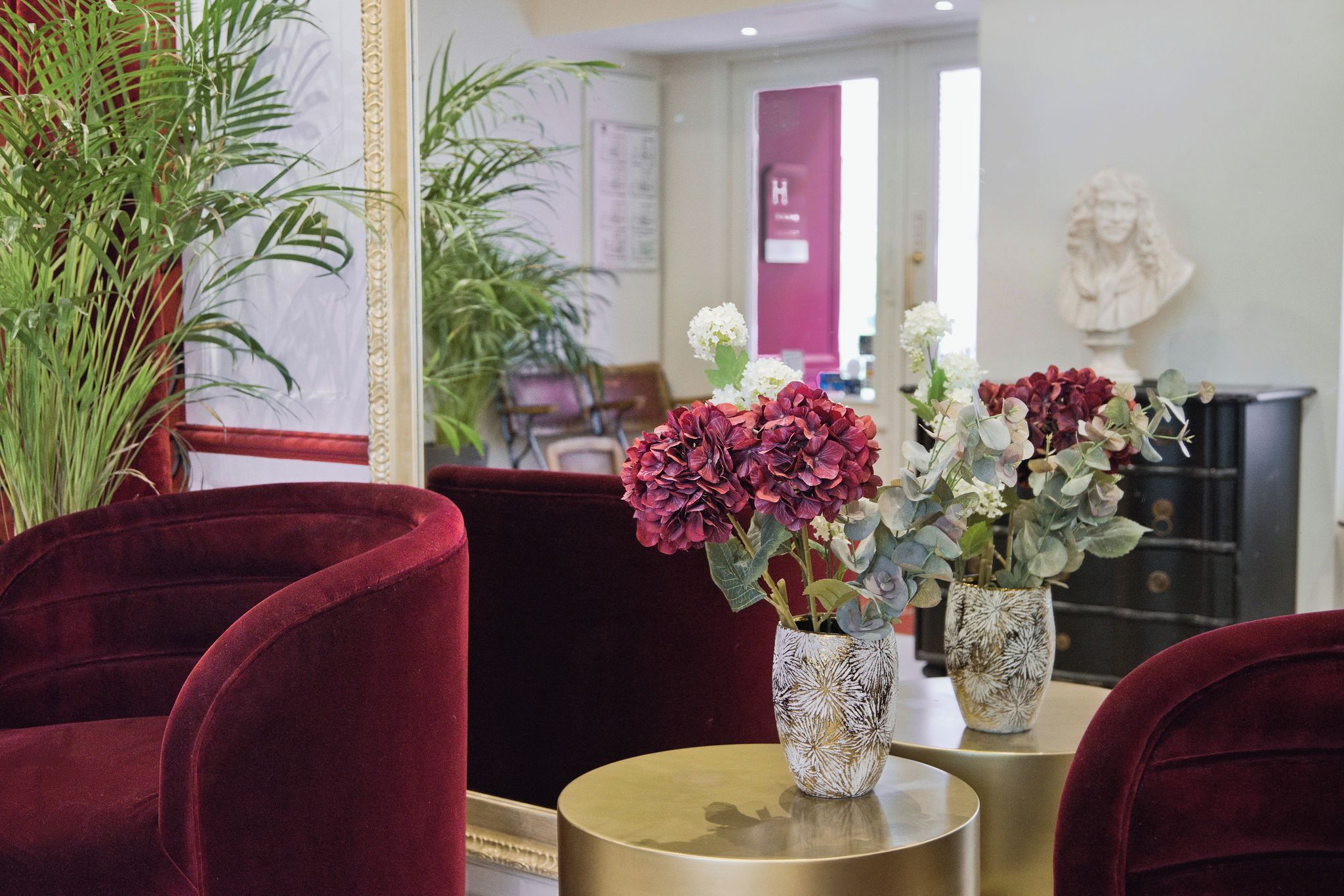 A room with red velvet chairs, a gold table, and two vases with flowers.