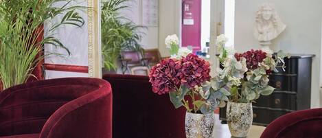 A room with red velvet chairs, a gold table, and two vases with flowers.