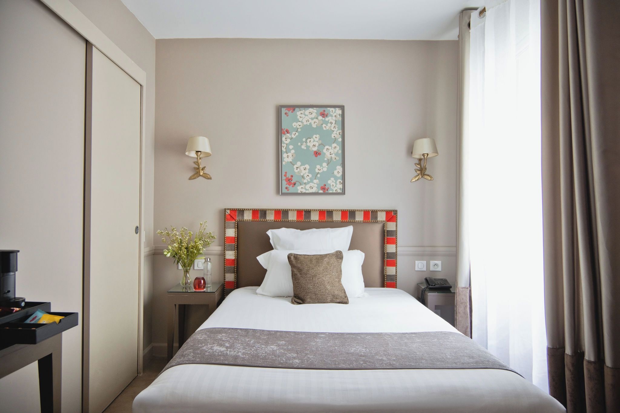 Een hotelkamer met een bed, nachtkastjes, een lamp, een lijst met bloemkunst en een telefoon.