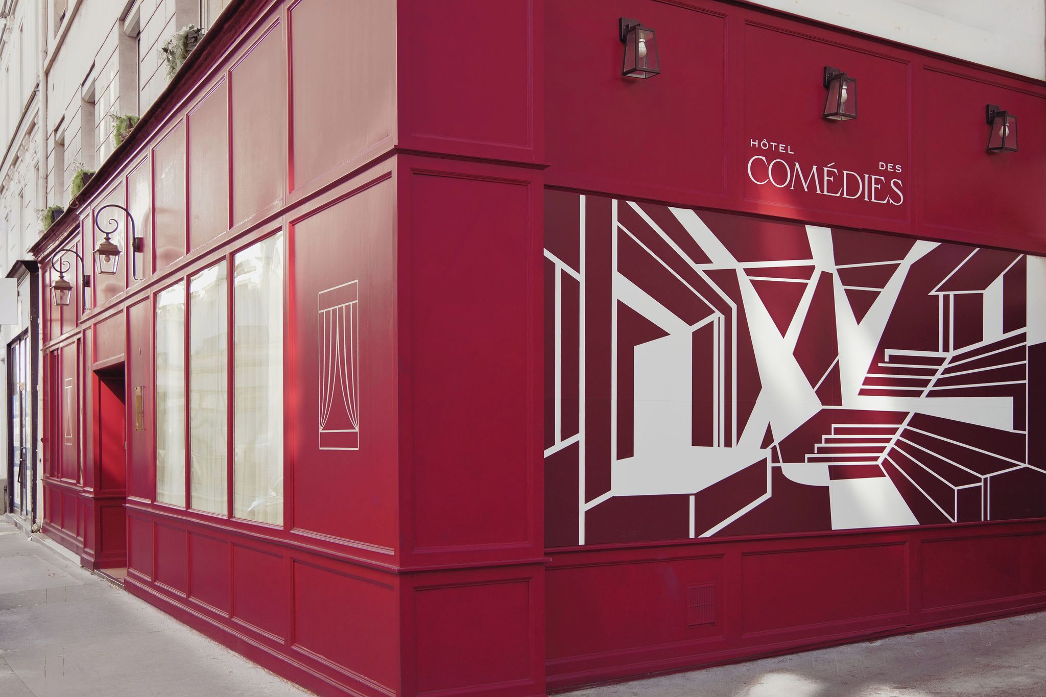 Un bâtiment rouge orné d’un grand motif géométrique sur la façade, avec l’inscription « Hôtel des COMÉDIES ».