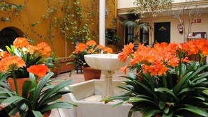 Een binnenplaats met een witte fontein, omringd door oranje bloemen en potplanten.