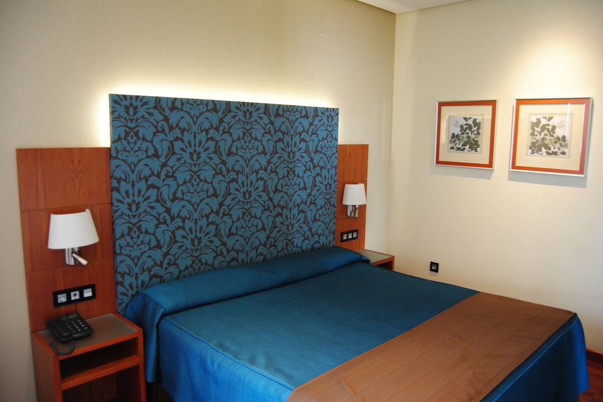 A hotel room with a large bed, two bedside tables with lamps, a wooden headboard, and two framed pictures on the wall.