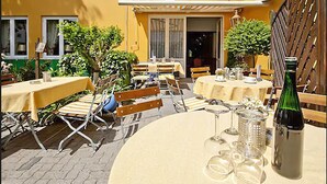 Eine Terrasse im Freien mit runden Tischen und Stühlen, einer Champagnerflasche und einem kleinen Garten mit Blumentöpfen.