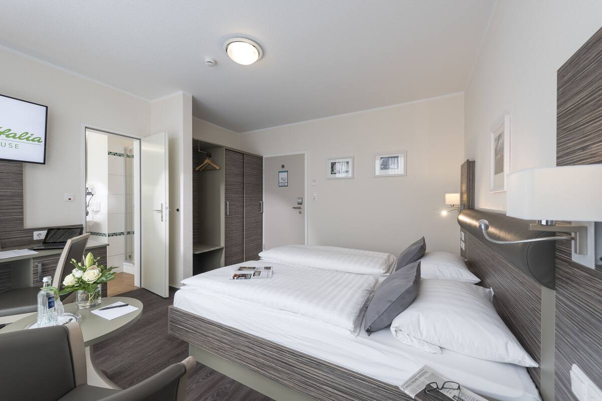A hotel room with a bed, a desk with a laptop, a chair, and a TV on the wall.